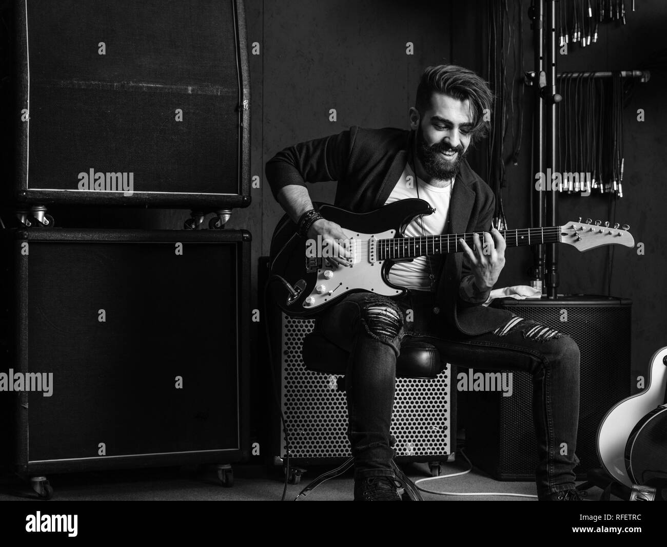 Foto in bianco e nero di un uomo con la barba seduto e a suonare la chitarra elettrica in uno studio di registrazione. Foto Stock