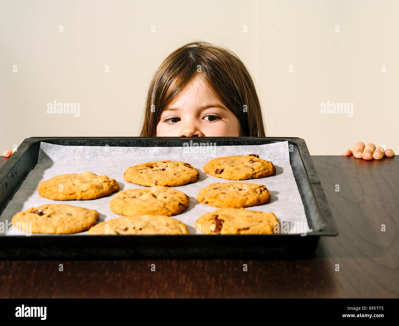 Foto di una ragazza giovane fissando un vassoio di calda i biscotti al cioccolato appena fuori dal forno. Foto Stock