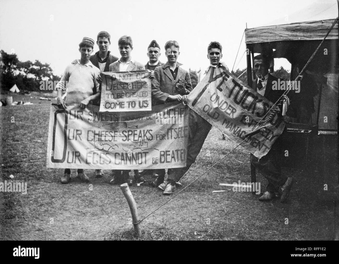 Uno dei primi anni del ventesimo secolo fotografia in bianco e nero che mostra un gruppo di ragazzi in un campeggio in Inghilterra, pubblicità il cibo e produrre essi hanno istituito in un negozio di dolciumi, sono titolari di banner per la pubblicità delle merci, con divertenti le didascalie. Foto Stock