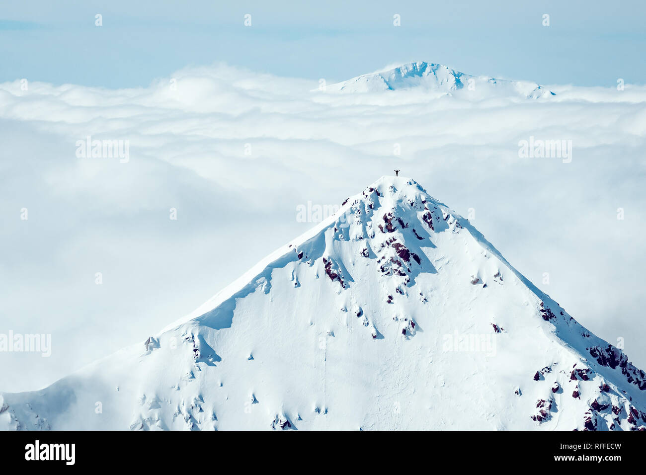 Un scalatore stanting sulla cima di una montagna lontana in inverno Foto Stock