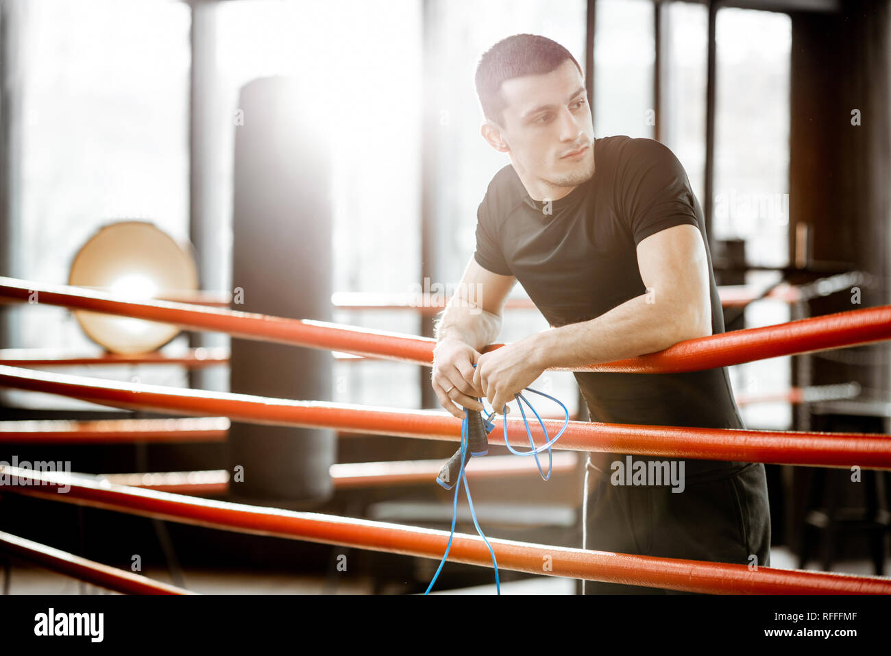 Ritratto di un giovane uomo atletico in abbigliamento sportivo nero in piedi sull'anello boxxing in palestra Foto Stock
