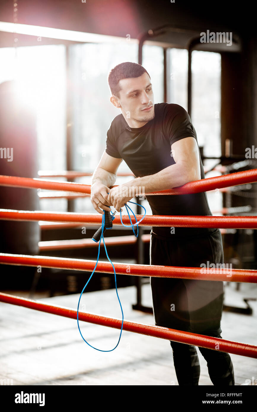 Ritratto di un giovane uomo atletico in abbigliamento sportivo nero in piedi sull'anello boxxing in palestra Foto Stock