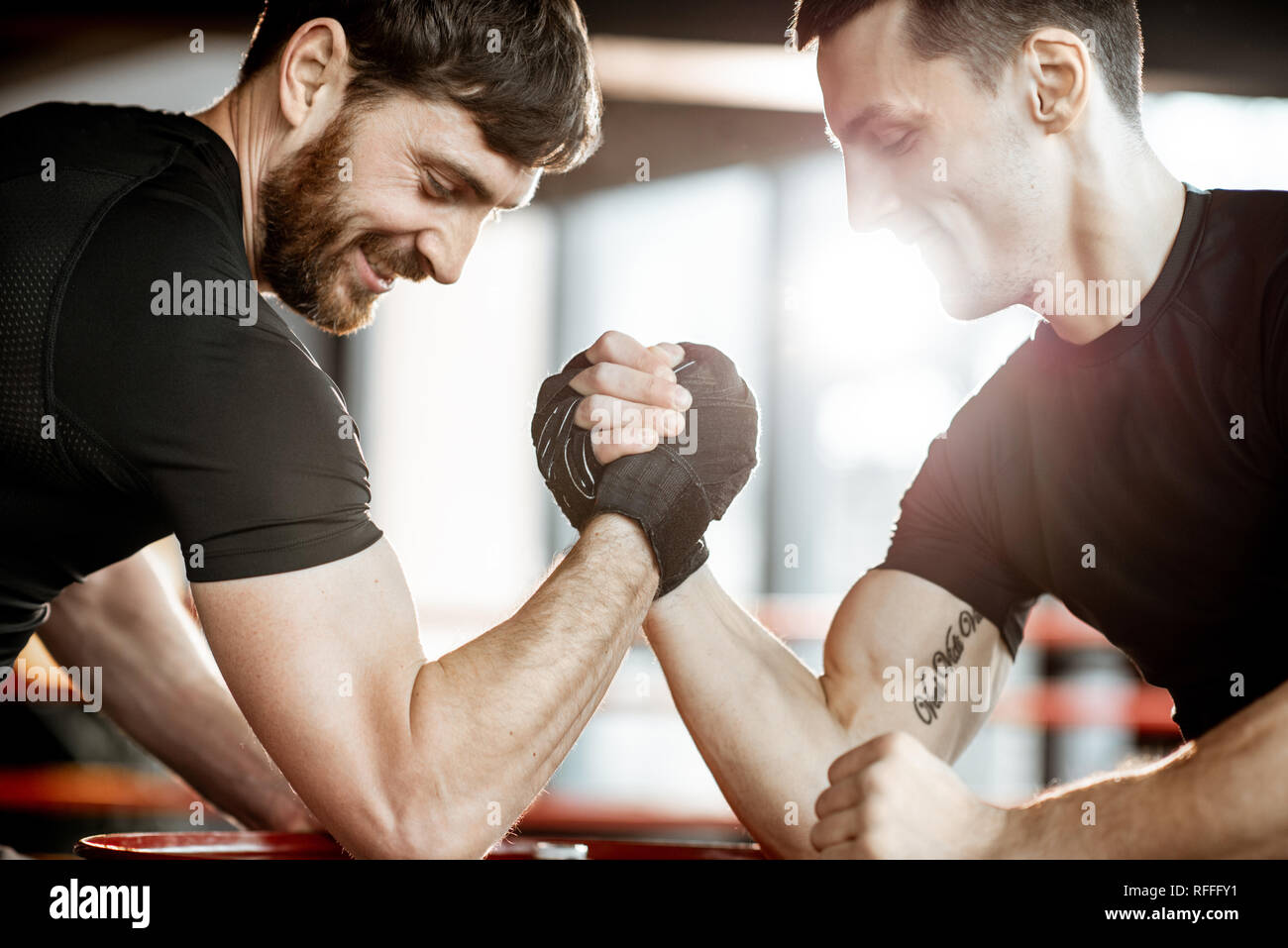 Due giovani atleti in abbigliamento sportivo nero avente un braccio rigido wrestling concorrenza su una canna rosso in palestra Foto Stock