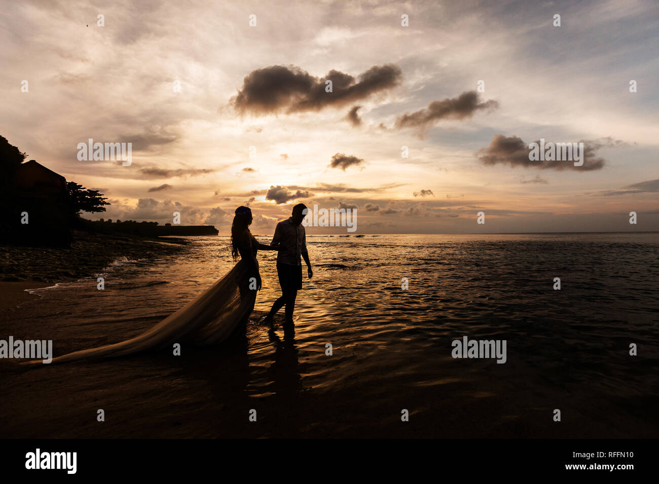 Sagome dello sposo e della sposa vanno mano nella mano sulla spiaggia sulla spiaggia al tramonto Foto Stock