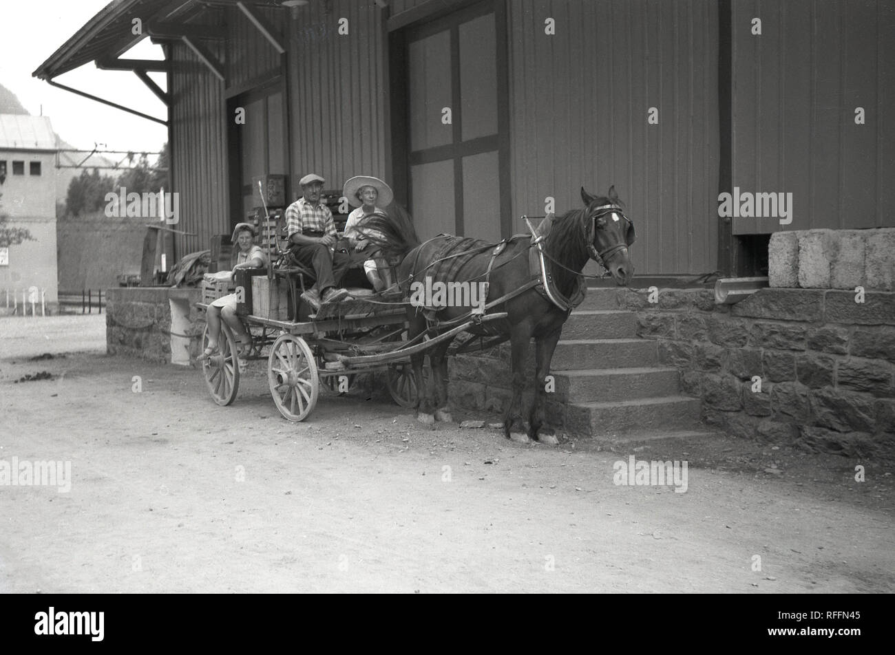 1947, storico, tre membri della locale famiglia contadina ubicazione su un cavallo e il carrello al di fuori di un deposito su di una pista nelle montagne svizzere. Foto Stock
