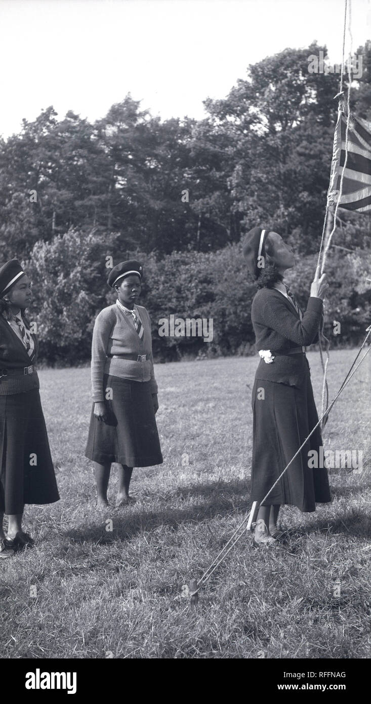 Degli anni Cinquanta, storico, tre inglesi Girl Guides in uniforme al di fuori di un campo mettendo un Union-Jack bandiera al loro campeggio, Inghilterra, Regno Unito. La ragazza di GUID sono state ufficialmente creata nel 1910 due anni dopo la creazione del Movimento Scout. Foto Stock