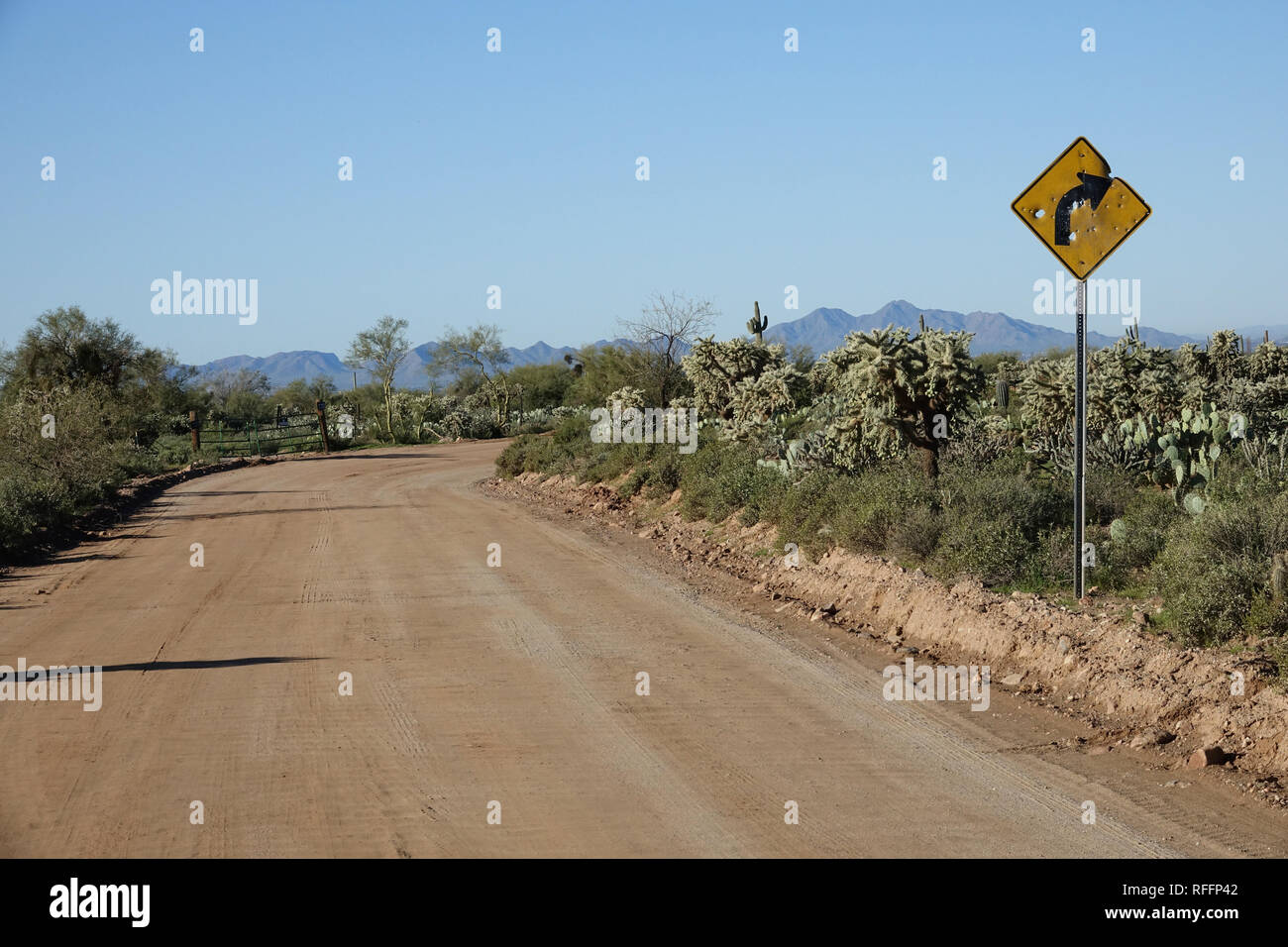 Un segno di segnalazione di curva su una strada sterrata nel deserto di Phoenix è perforata con fori di proiettile. Foto Stock
