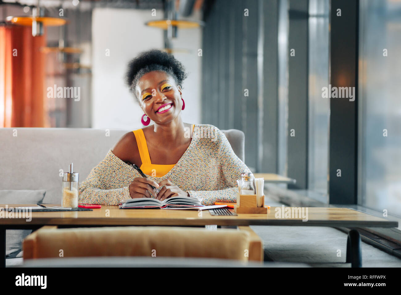 Smart studente sorridere mentre facendo alcune note nella caffetteria Foto Stock