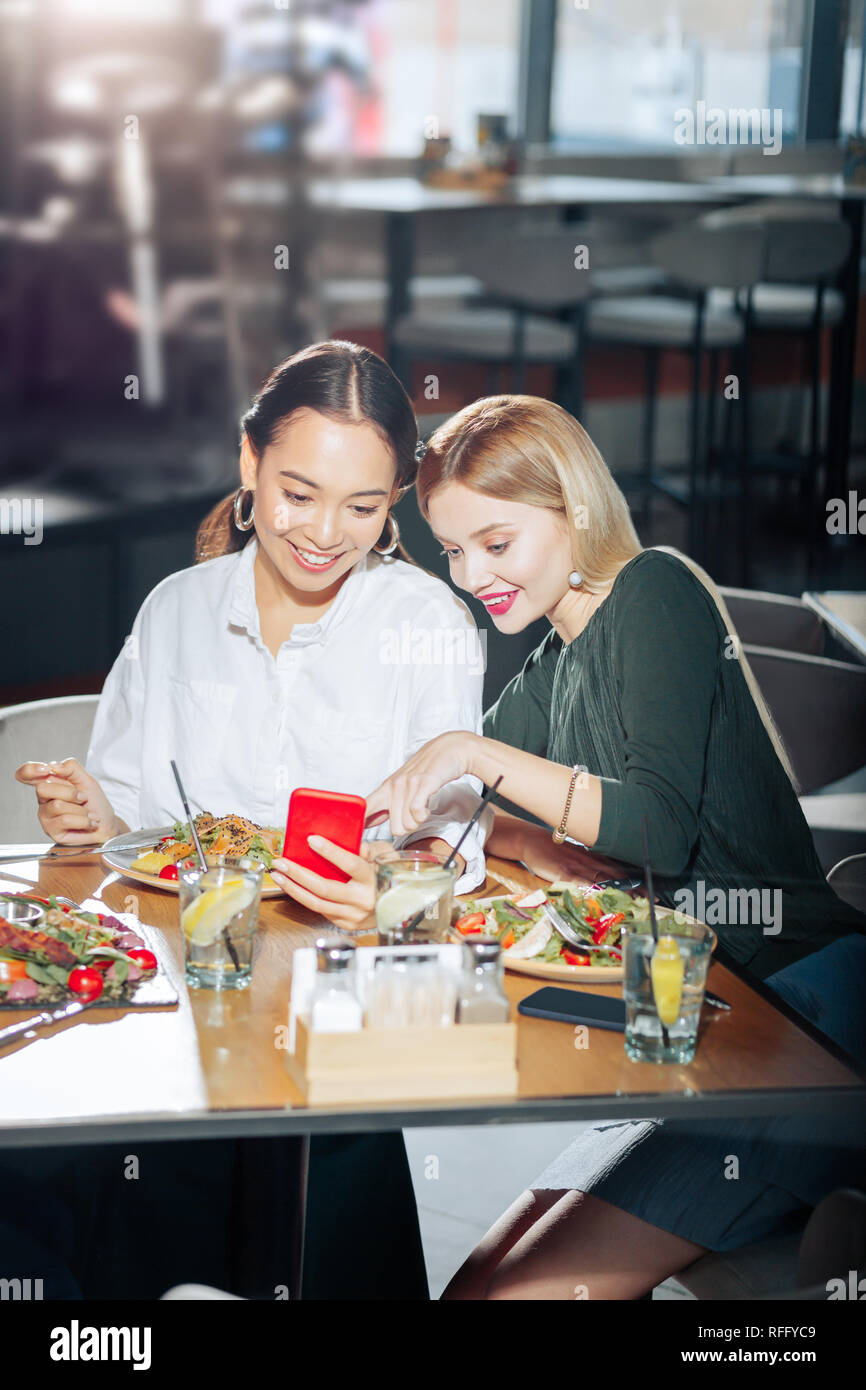 Due migliori amici newsfeed di lettura su smartphone rosso durante la cena Foto Stock