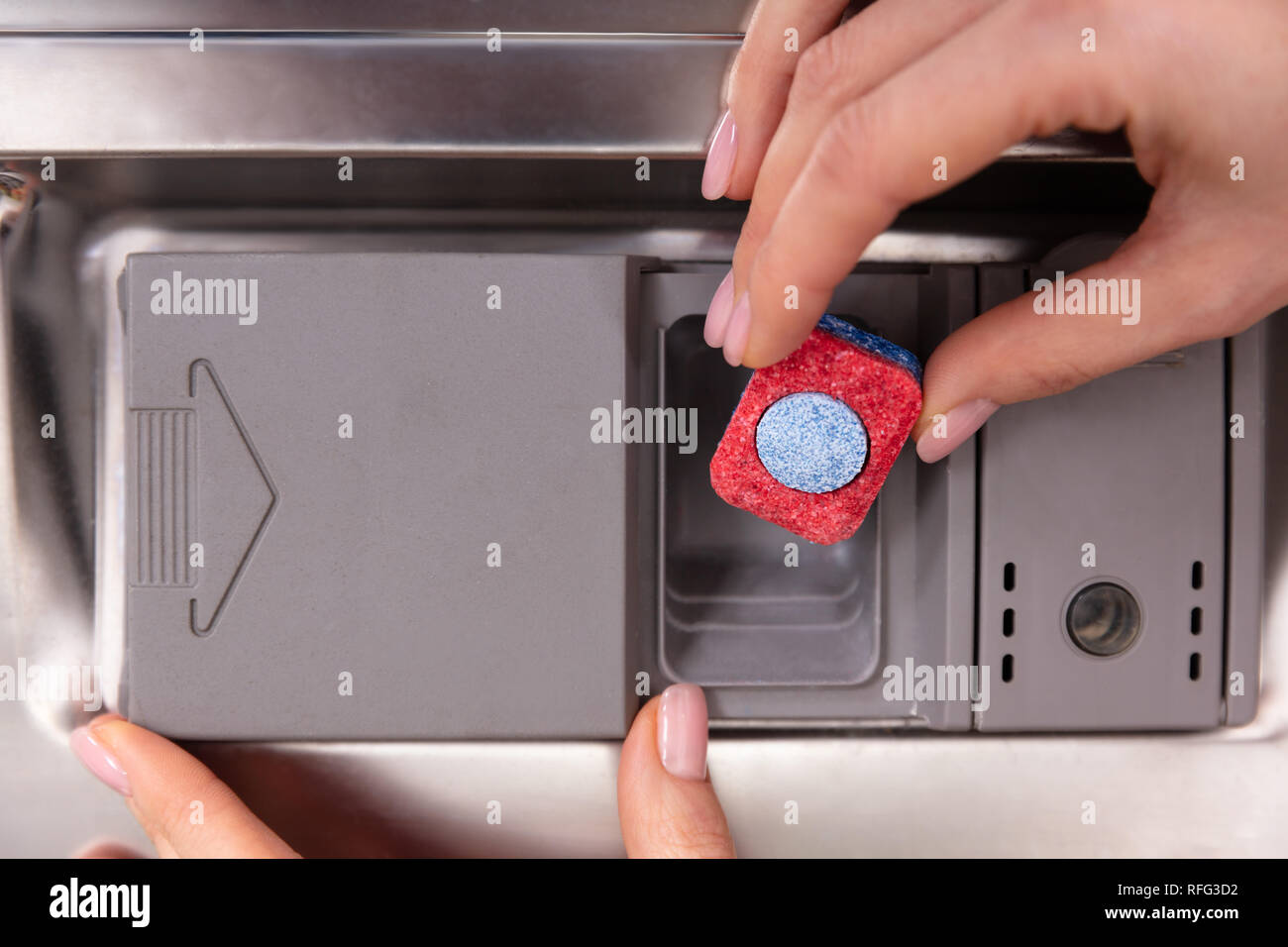 Mano umana mettendo il rosso e il blu di sapone colorato compressa nella fessura di lavastoviglie Foto Stock