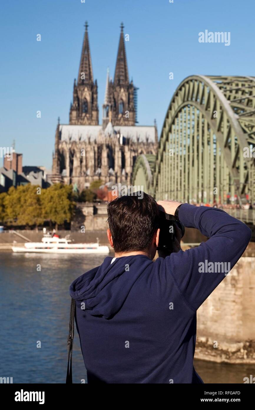 Un uomo fotografie del duomo di Colonia con il ponte di Hohenzollern, Colonia, nella Renania settentrionale-Vestfalia, Germania Foto Stock