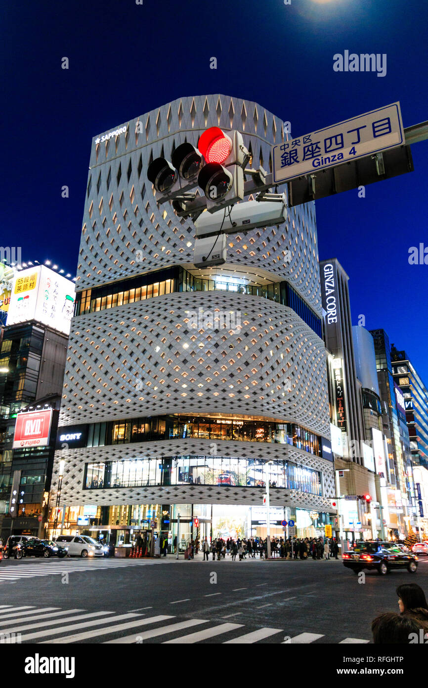 Il bianco Ginza luogo di costruzione in alluminio e la sua facciata del pannello. Di notte, la strada che attraversa in primo piano con Ginza 4 segno e luce di stop rossa. Il traffico. Foto Stock