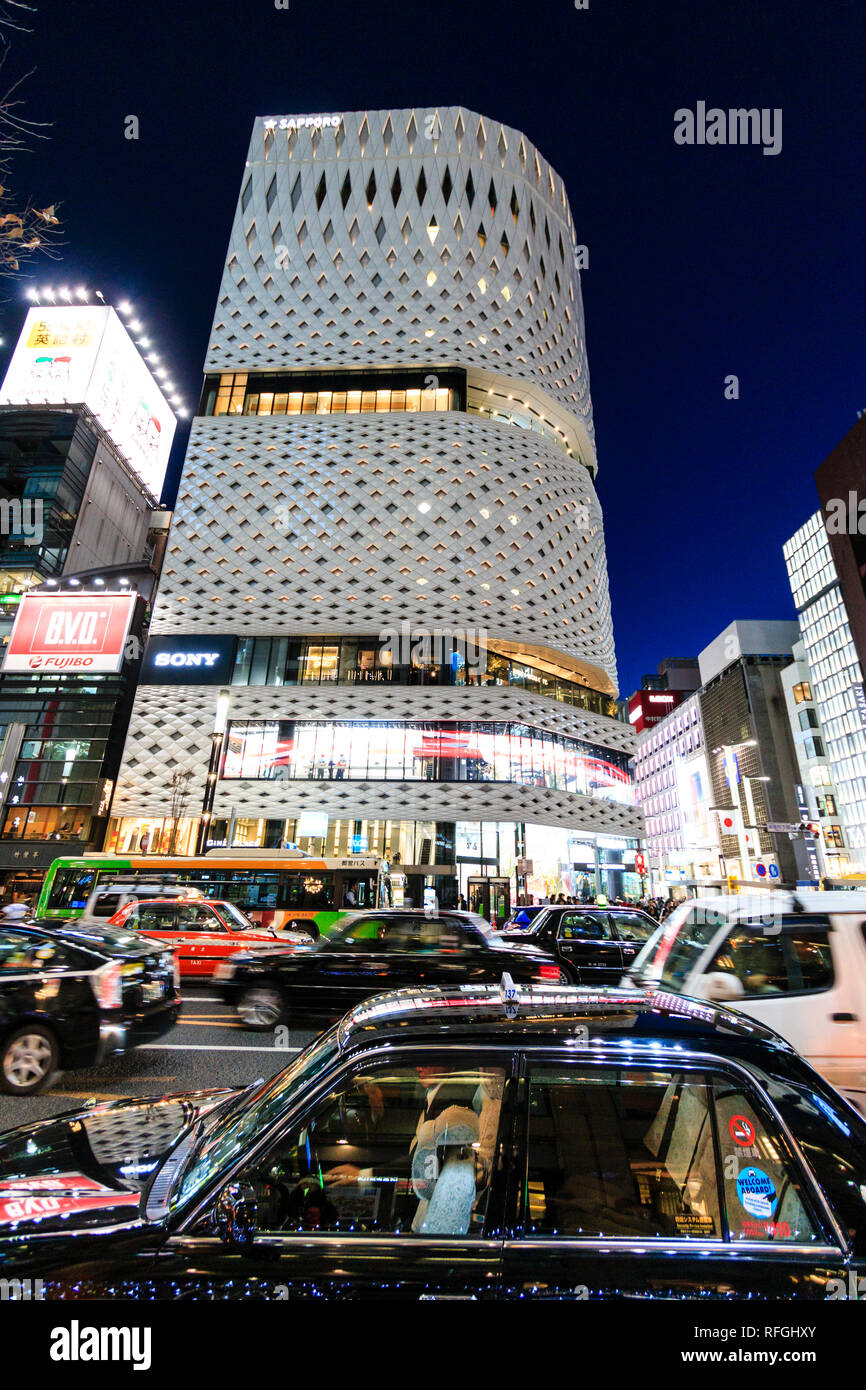 Il bianco Ginza luogo di costruzione in alluminio e la sua facciata del pannello illuminato di notte tempo. Primo piano, parcheggiati taxi, vernice riflettente luci di costruzione. Foto Stock