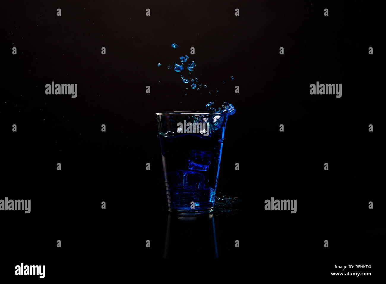 Vetro bevanda blu schizzi fuori. Colpo contro nero superficie riflettente. Bevanda isolato shot su sfondo nero. Copia dello spazio disponibile Foto Stock