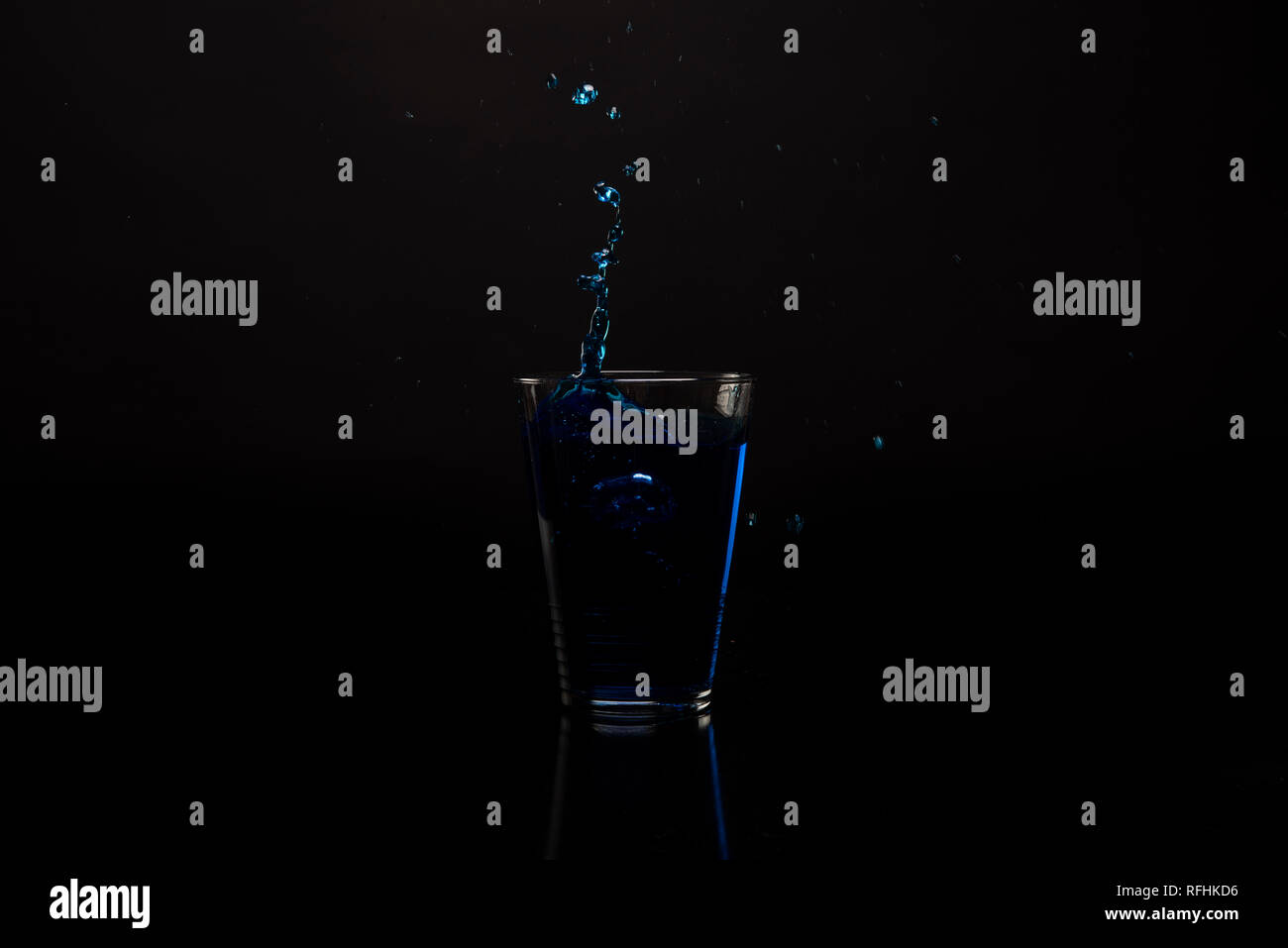 Vetro bevanda blu schizzi fuori. Colpo contro nero superficie riflettente. Bevanda isolato shot su sfondo nero. Copia dello spazio disponibile Foto Stock
