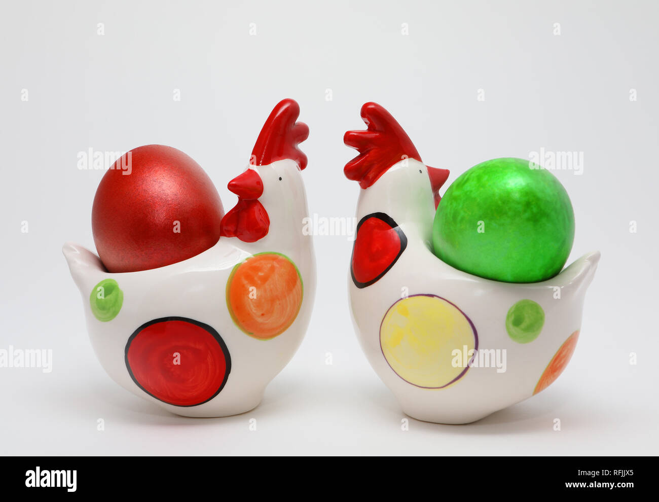 Due colorate uova di Pasqua colori rosso e verde in due galline giocattolo su sfondo bianco, la molla dell'immagine. Concetto di pasqua. Foto Stock