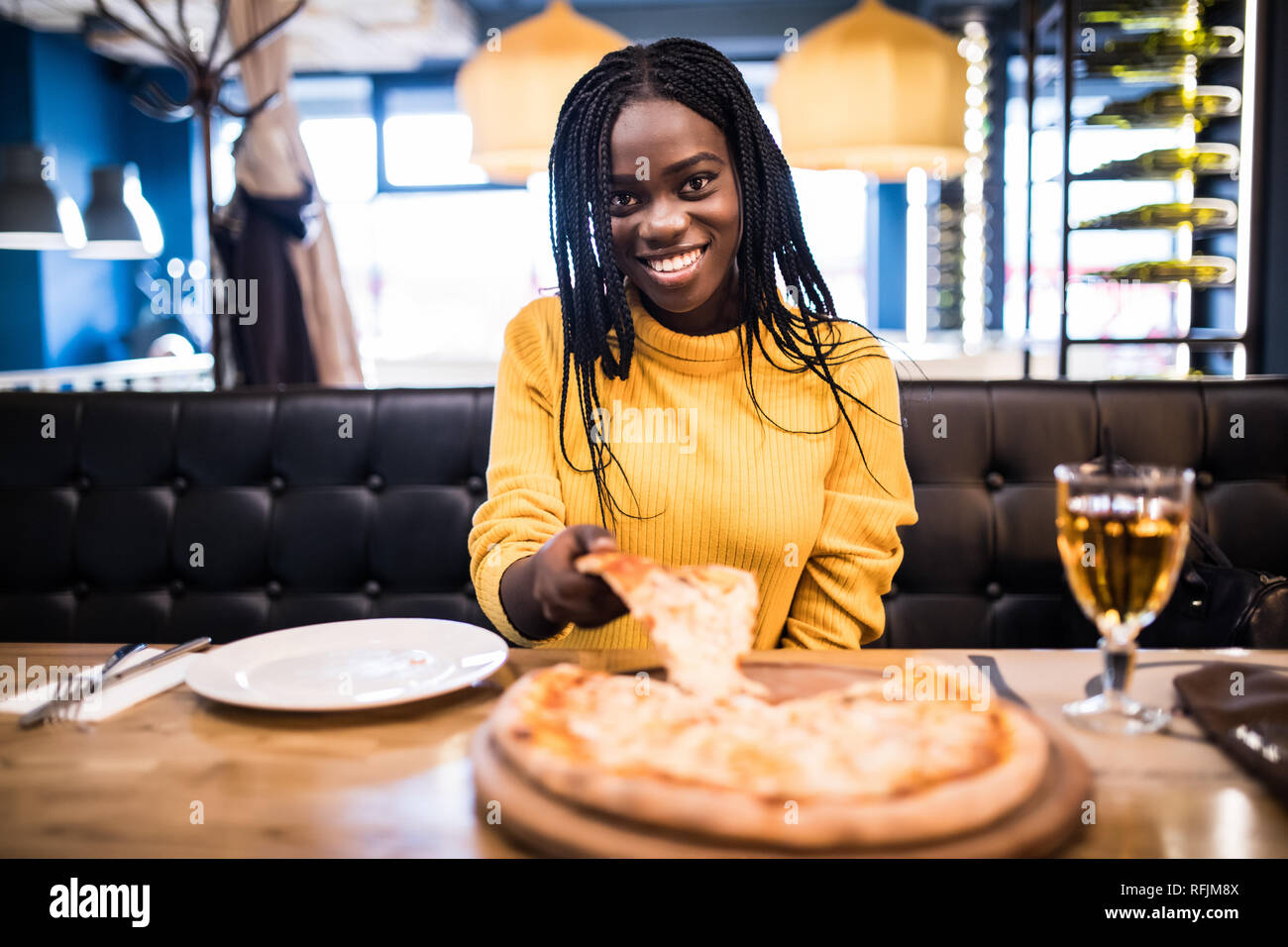 Giovane ragazza africana in maglione giallo mangiare la pizza al ristorante  Foto stock - Alamy