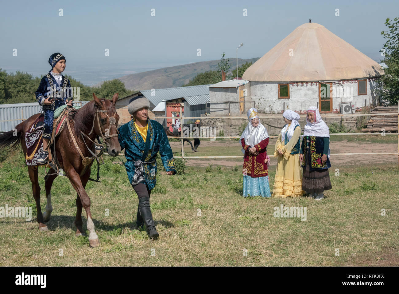 Madre kazaka e nonne guardare un giovane ragazzo di imparare a guidare un cavallo, Almaty, Kazakhstan Foto Stock