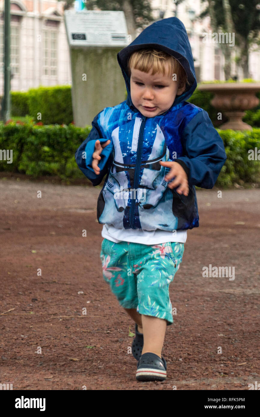 Un grave 2 anno vecchio toddler indossando un blue star wars themed la giacca è in esecuzione sulla strada del centro cittadino di San Jose, Costa Rica Foto Stock