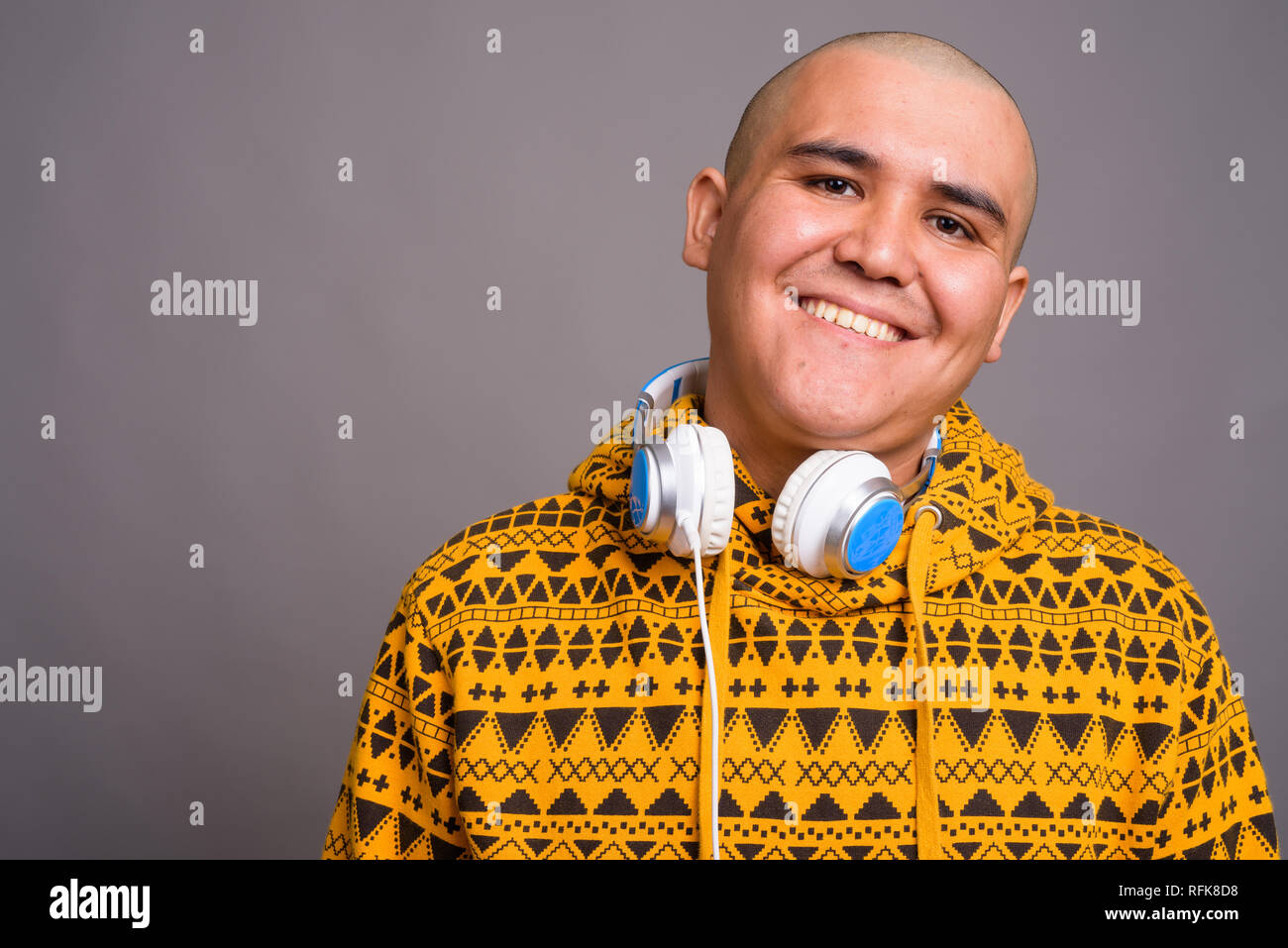 Giovani bald uomo asiatico che indossano le cuffie contro uno sfondo grigio Foto Stock