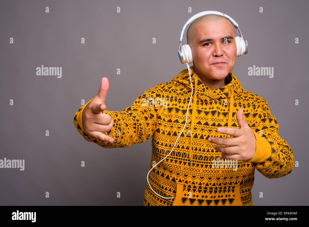 Giovani bald uomo asiatico ascoltando musica contro lo sfondo grigio Foto Stock