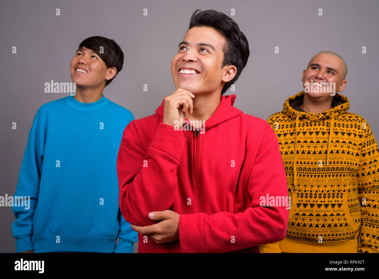 Tre giovani uomini asiatici di indossare abiti caldi contro backgro grigio Foto Stock