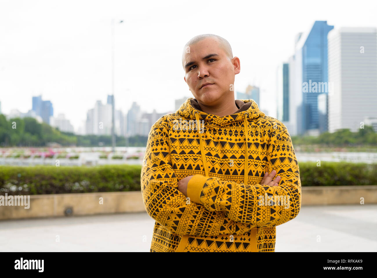 Giovani asiatici calvo uomo contro la vista della città al parco Foto Stock