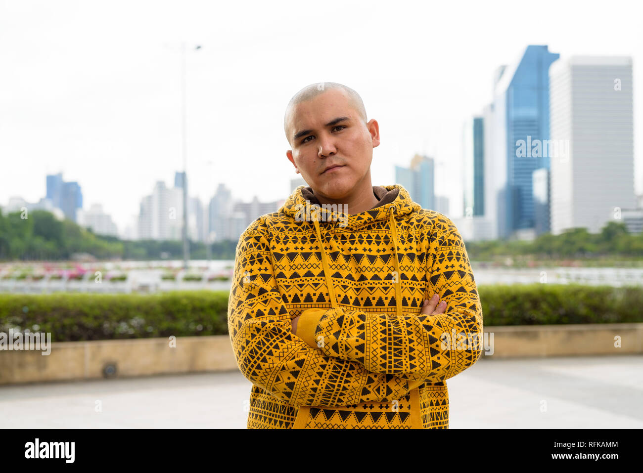 Giovani asiatici calvo uomo contro la vista della città al parco Foto Stock