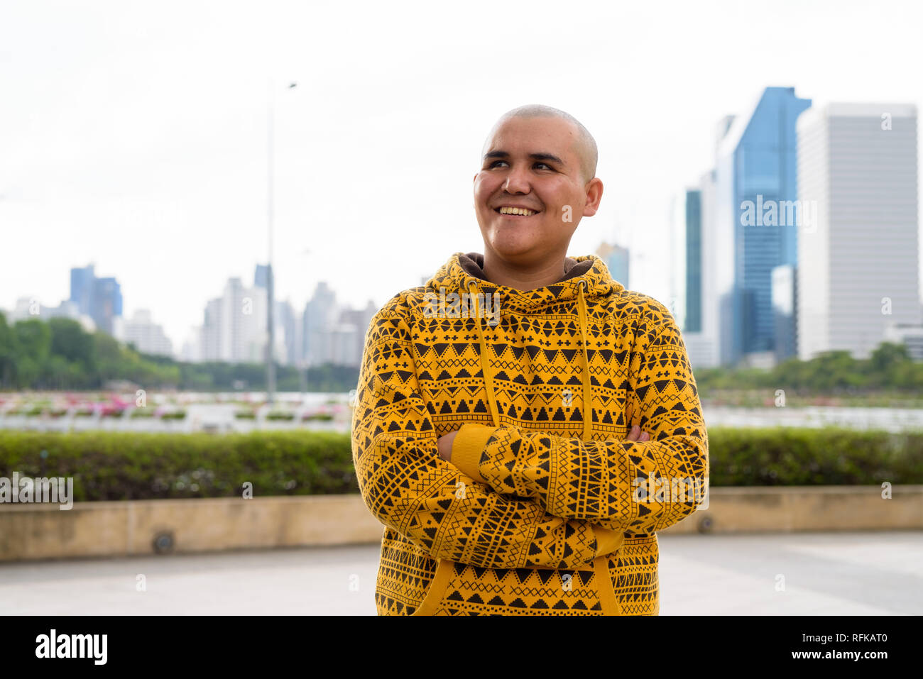 Giovani asiatici calvo uomo contro la vista della città al parco Foto Stock