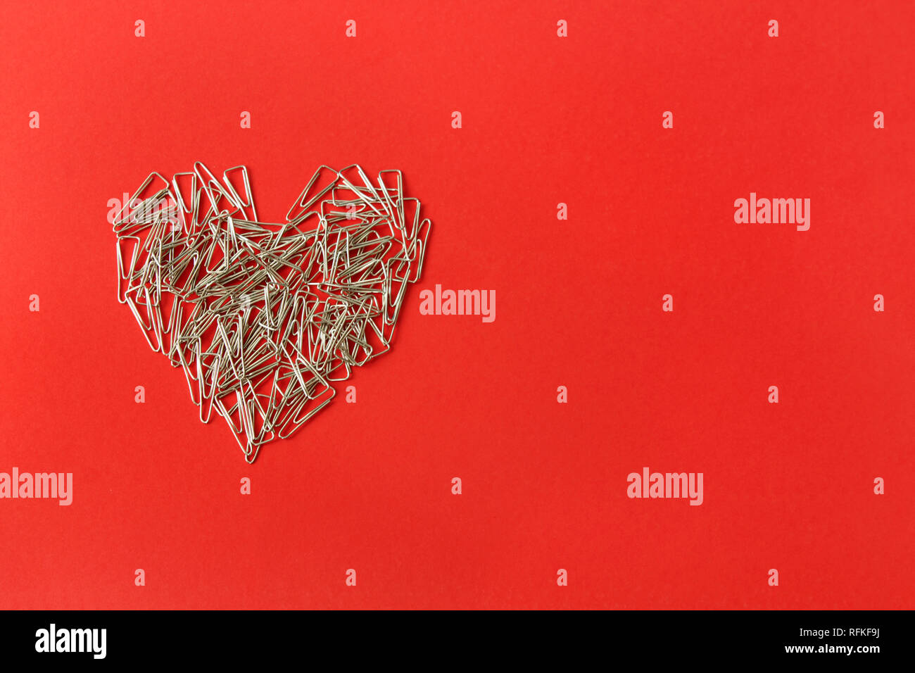 Cuore su uno sfondo di colore rosso. Il giorno di San Valentino. Il giorno di San Valentino biglietto di auguri. Cuore di clip di carta. Articoli di cancelleria. Foto Stock