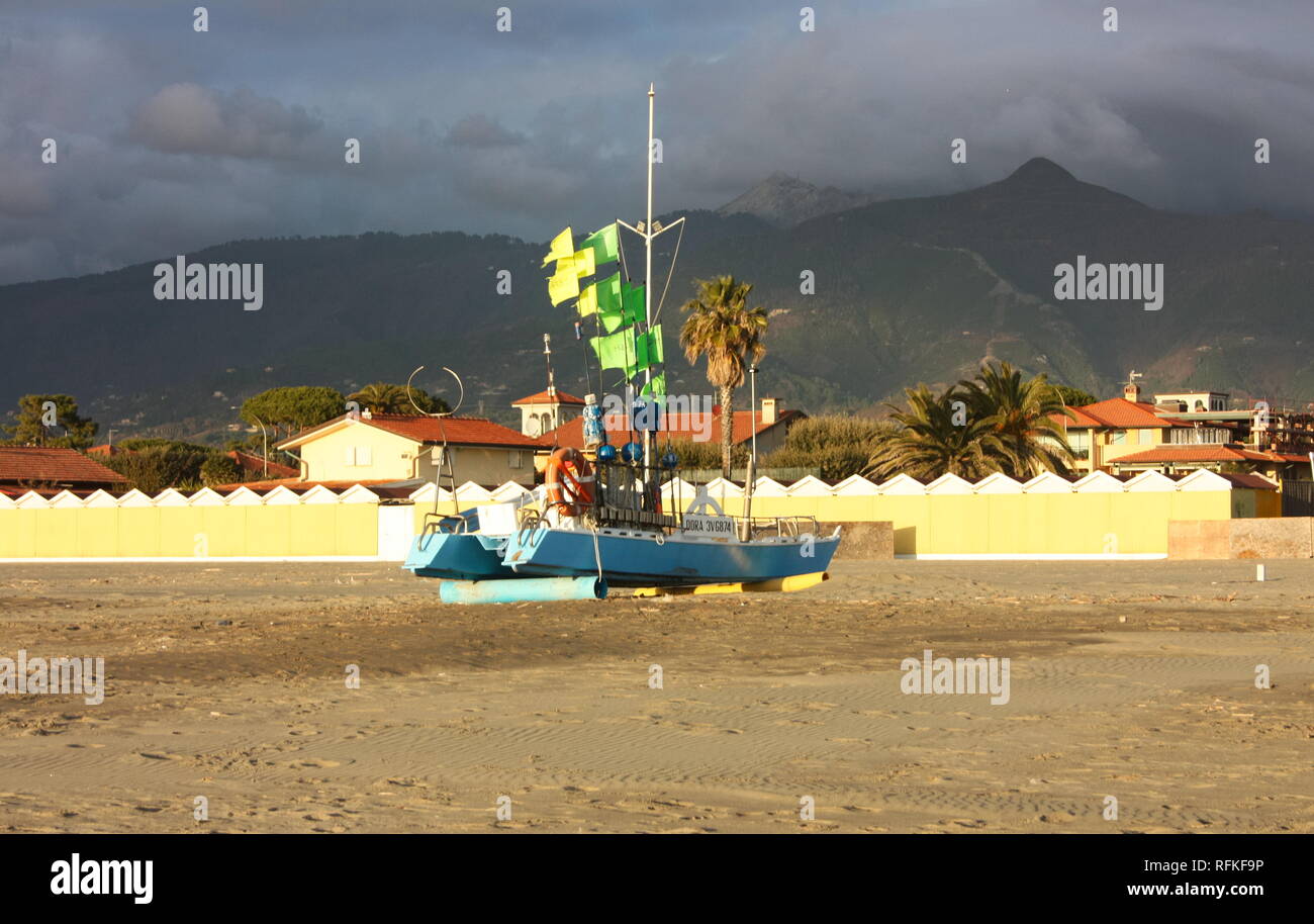 Barca verde con bandiere illuminate dal sole. Gli immigrati sono sbarcati sulla spiaggia. il colorato in barca a filamento è sulla spiaggia Foto Stock