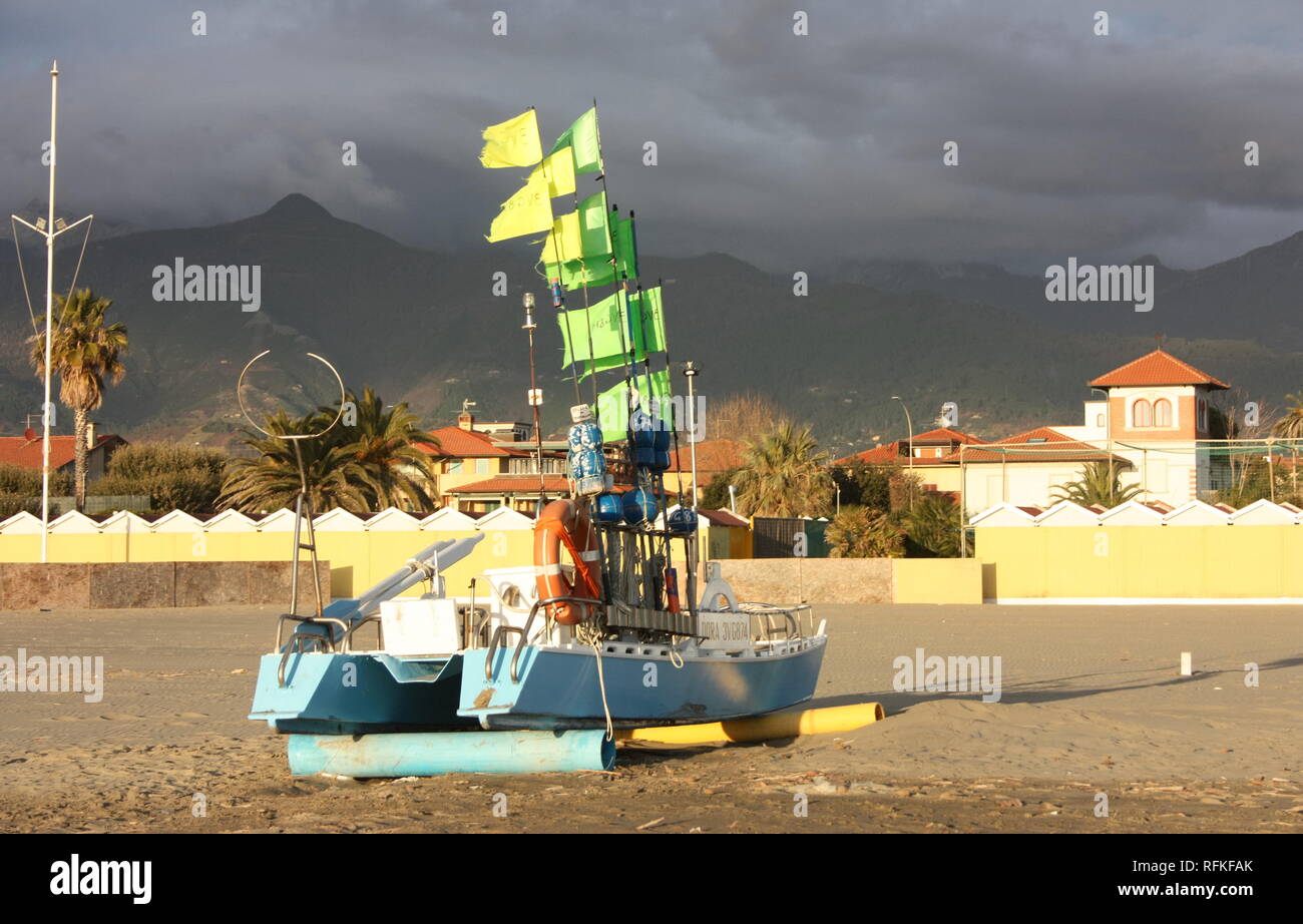 Barca verde con bandiere illuminate dal sole. Gli immigrati sono sbarcati sulla spiaggia. il colorato in barca a filamento è sulla spiaggia Foto Stock