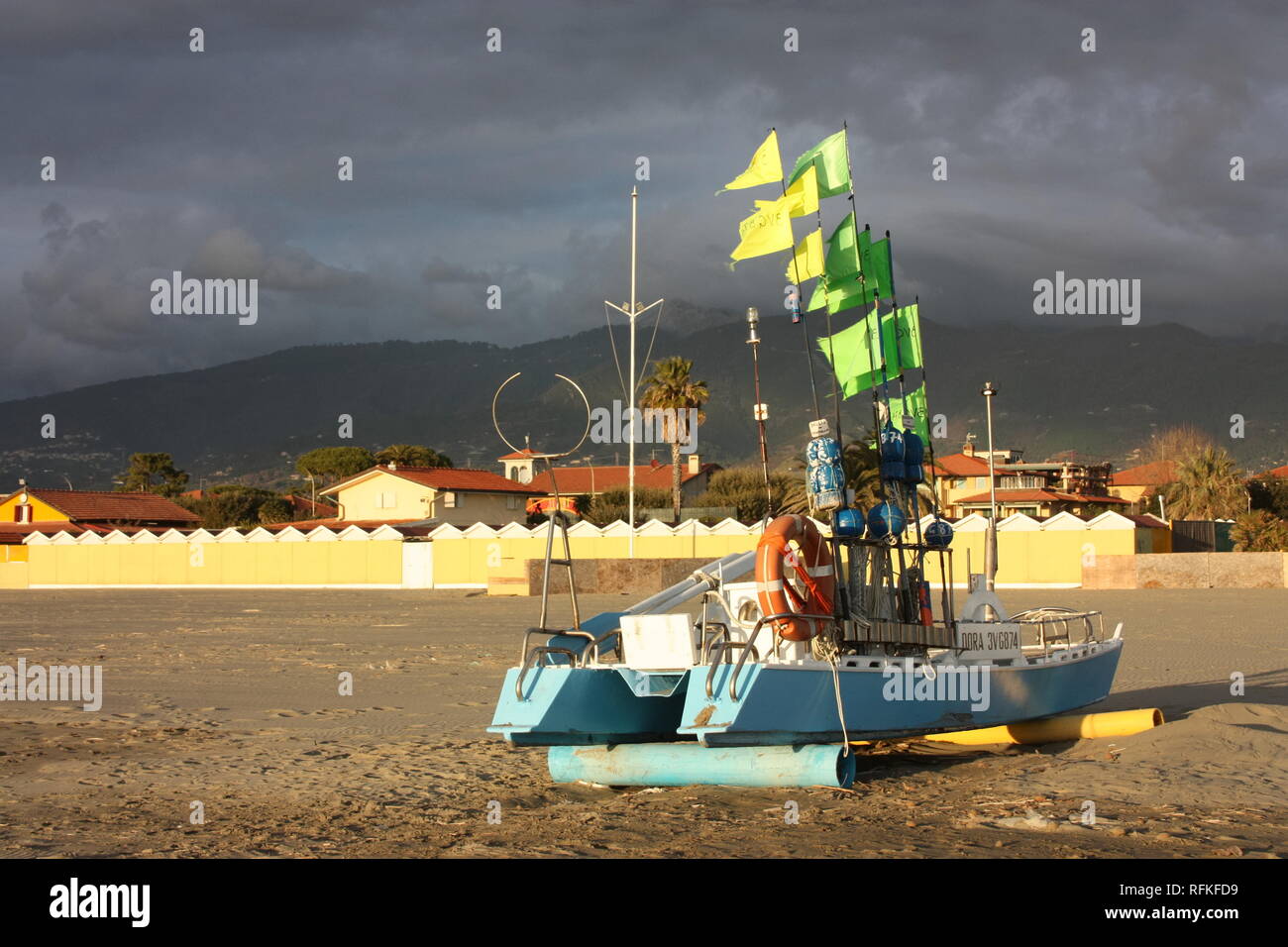 Barca verde con bandiere illuminate dal sole. Gli immigrati sono sbarcati sulla spiaggia. il colorato in barca a filamento è sulla spiaggia Foto Stock