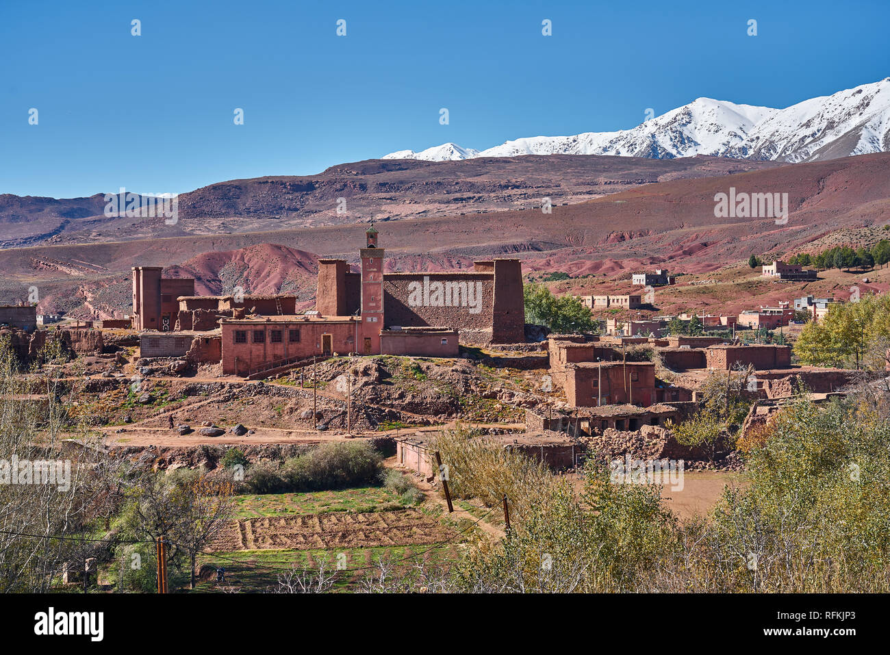 Tradizionale villaggio di mattoni di fango case moschea. Le montagne innevate dell'Atlante sono sul retro. Presa nei pressi di Ighrem N'Ougdal, provincia di Ouarzazate, Marocco Foto Stock