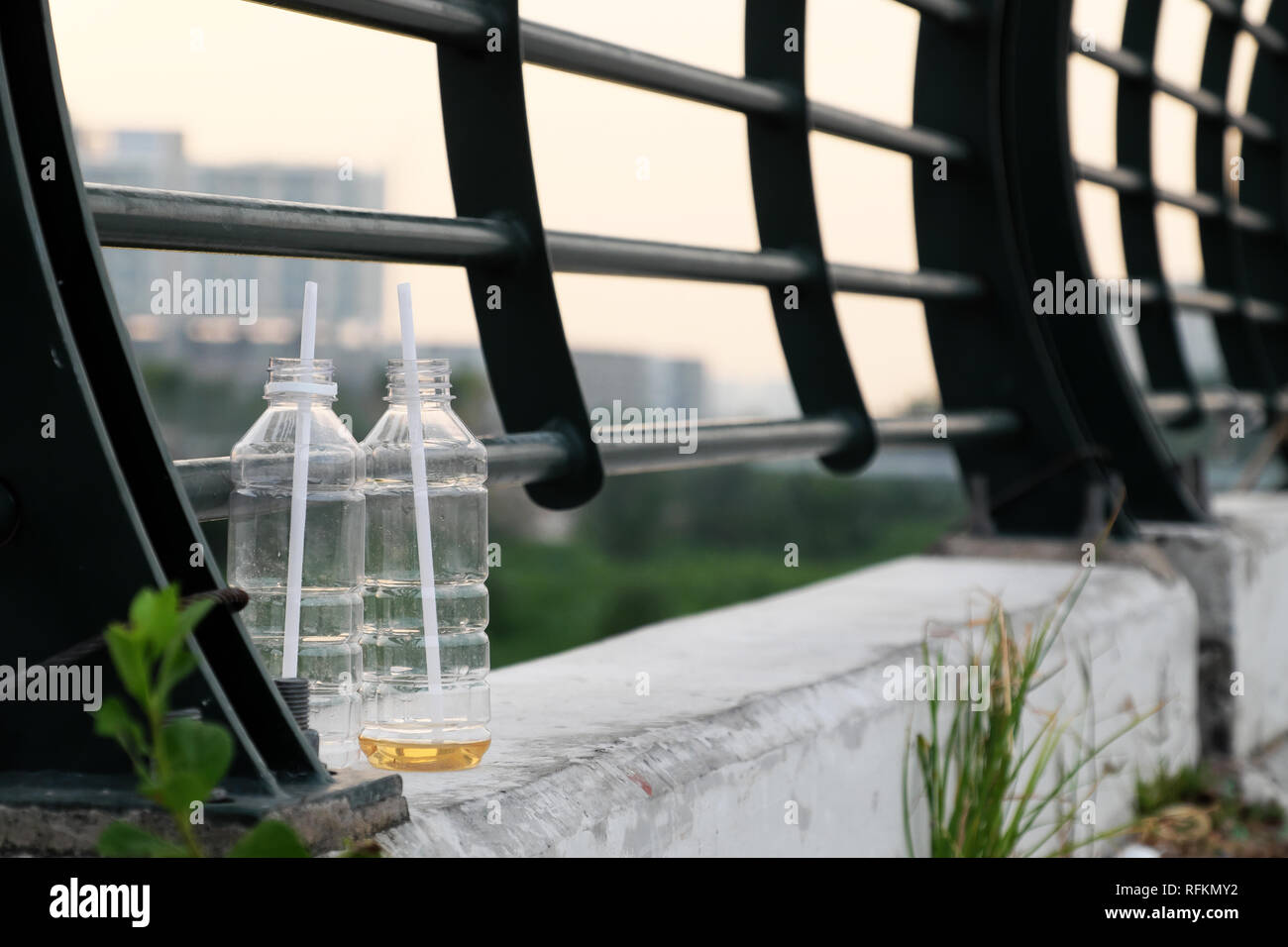 Due bottiglie di plastica con paglia e lasciare sulla ringhiera del ponte sulla strada urbana a Ho Chi Minh City, Vietnam, cattiva abitudine fare l'inquinamento ambientale, angolo basso Foto Stock