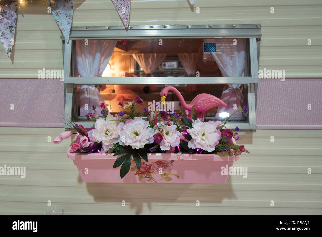 Un fenicottero rosa di plastica e i fiori di plastica in una cassetta per fiori su un piccolo stile retrò camper. Foto Stock