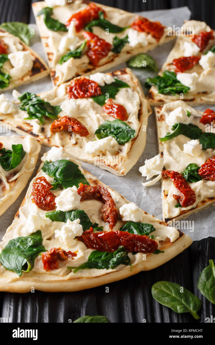 In Medio Oriente la pizza con hummus, pomodori secchi, spinaci e formaggio di capra vicino sul piano verticale. Foto Stock