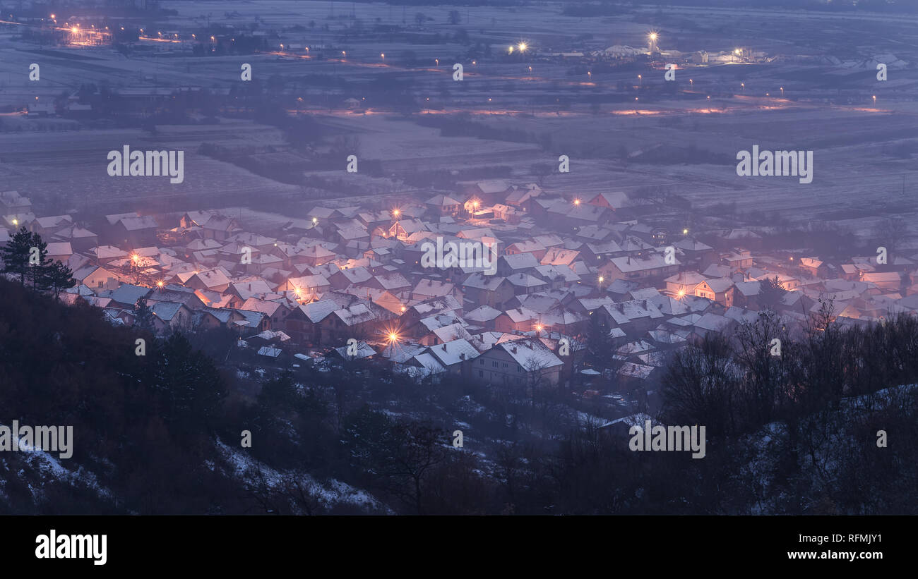 Vista da sopra di una sognante, misty piccolo paese coperto di neve durante la tarda ora blu Foto Stock