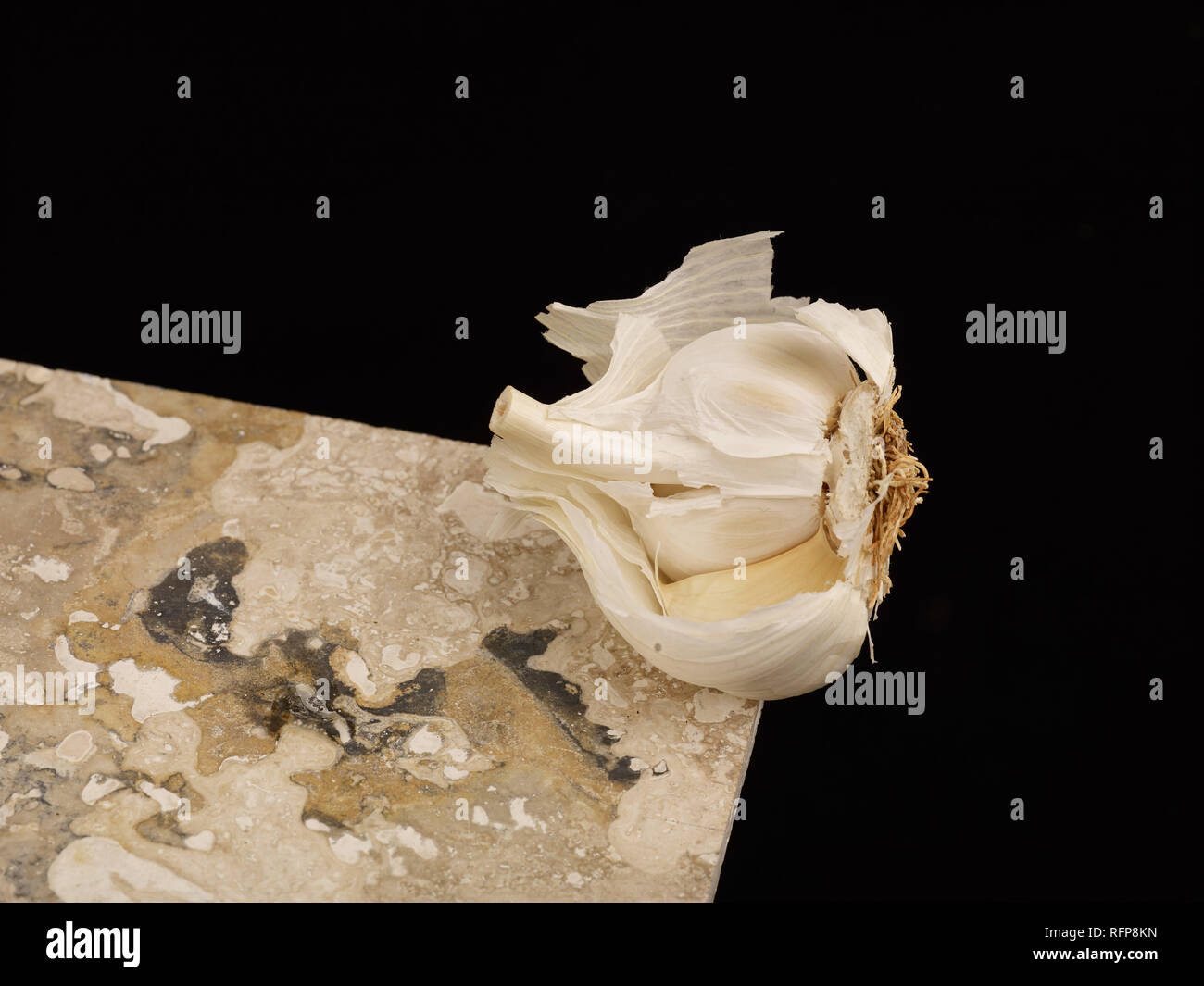 Spicchio di aglio bilanciato sul ripiano di marmo contro uno sfondo nero, alimento vegetale fotografia Foto Stock