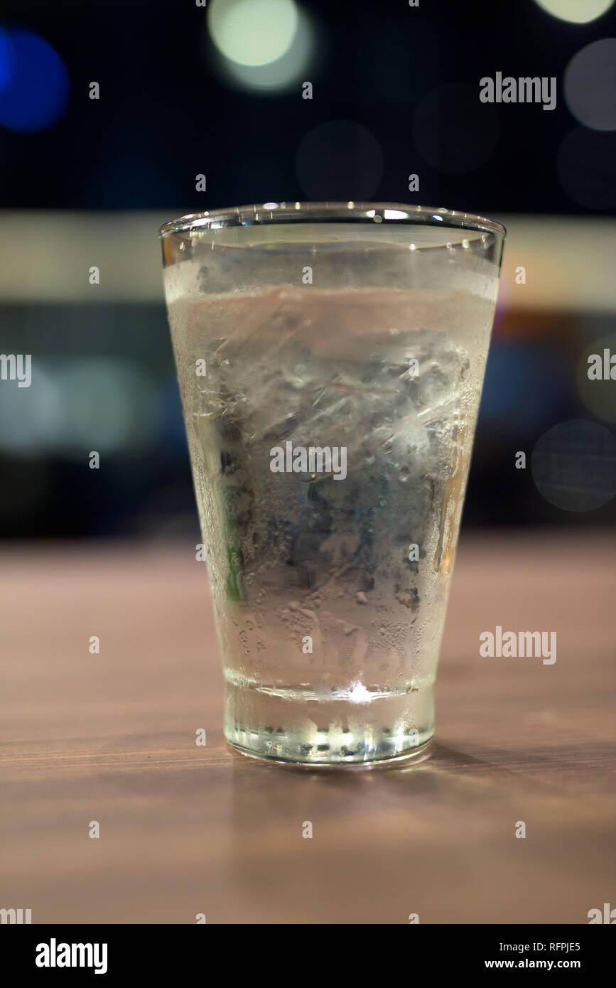 Bicchiere di acqua potabile in interni su tavola con lo sfondo della città di notte Foto Stock