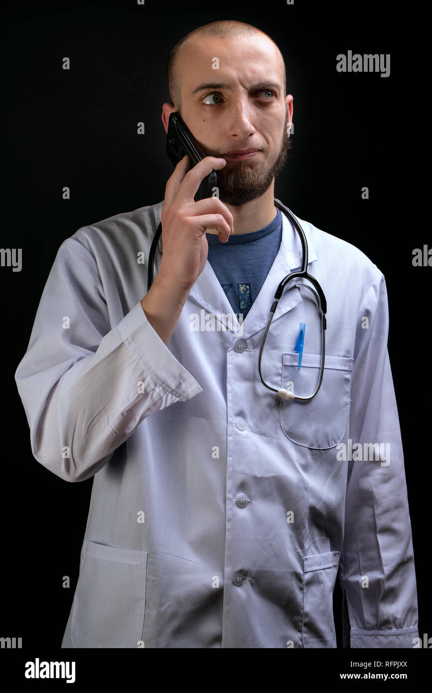 Medico di sesso maschile di parlare al telefono mentre avente il suo stetoscopio sulle spalle. Guardando lontano chiedendo dalla fotocamera Foto Stock