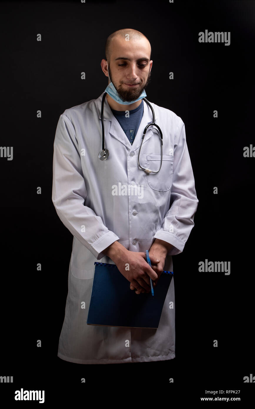 Medico maschio verticale con uno stetoscopio, maschera e tenendo premuto un file cercando triste. Prescription risultati visualizzati lontano dalla telecamera Foto Stock