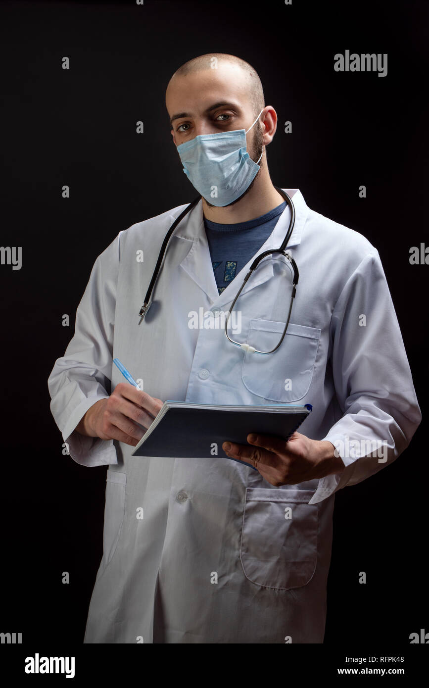Giovane maschio medico con stetoscopio, indossando maschera sul viso e tenendo un file mentre guardando la fotocamera. Business il concetto di assistenza sanitaria Foto Stock