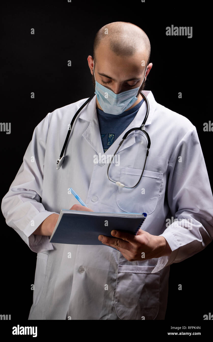Giovane maschio medico con stetoscopio, indossando maschera sul viso e la scrittura di un file prescrizione. Trattamento medico concept Foto Stock