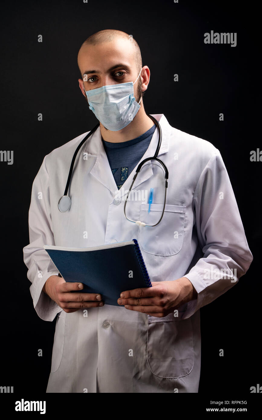 Giovane maschio medico con stetoscopio, indossando maschera sul viso e tenendo un file mentre guardando la fotocamera. Business il concetto di assistenza sanitaria Foto Stock