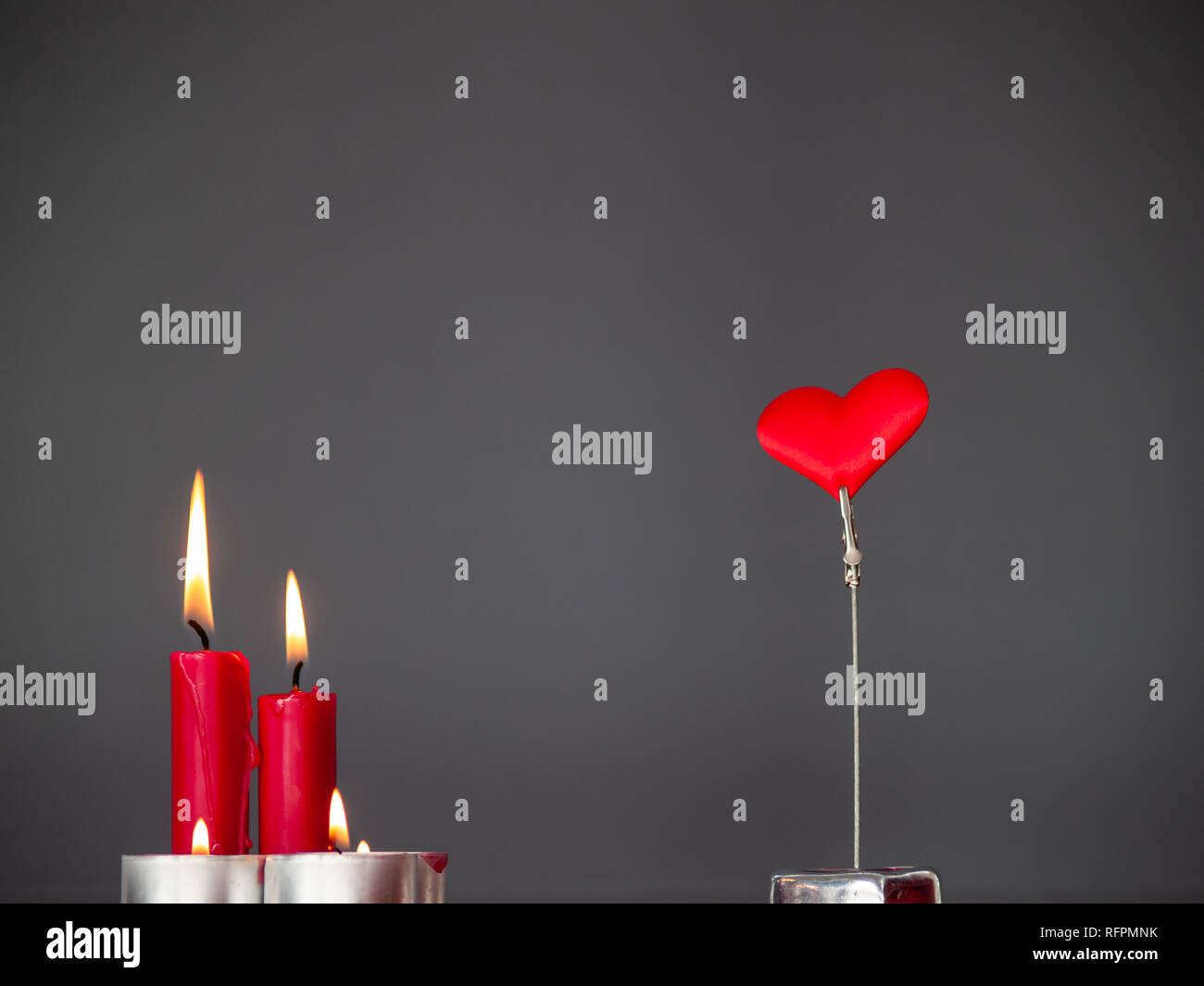 Concetto di amore candele rosse accese e un cuore rosso con sfondo grigio Foto Stock