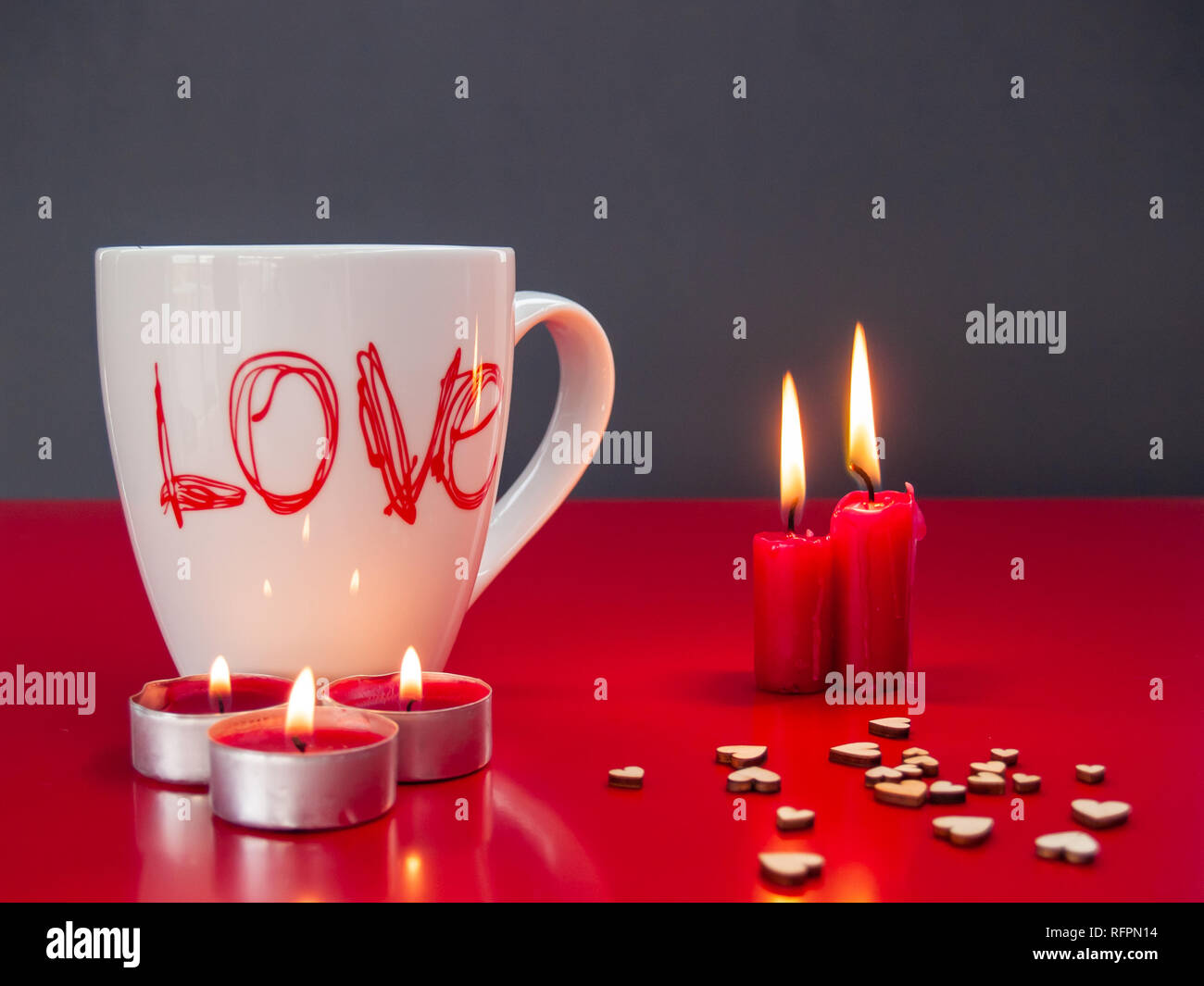 Concetto di amore ancora vita con rosso acceso candele e una colazione cup con la parola amore e piccoli cuori di legno Foto Stock