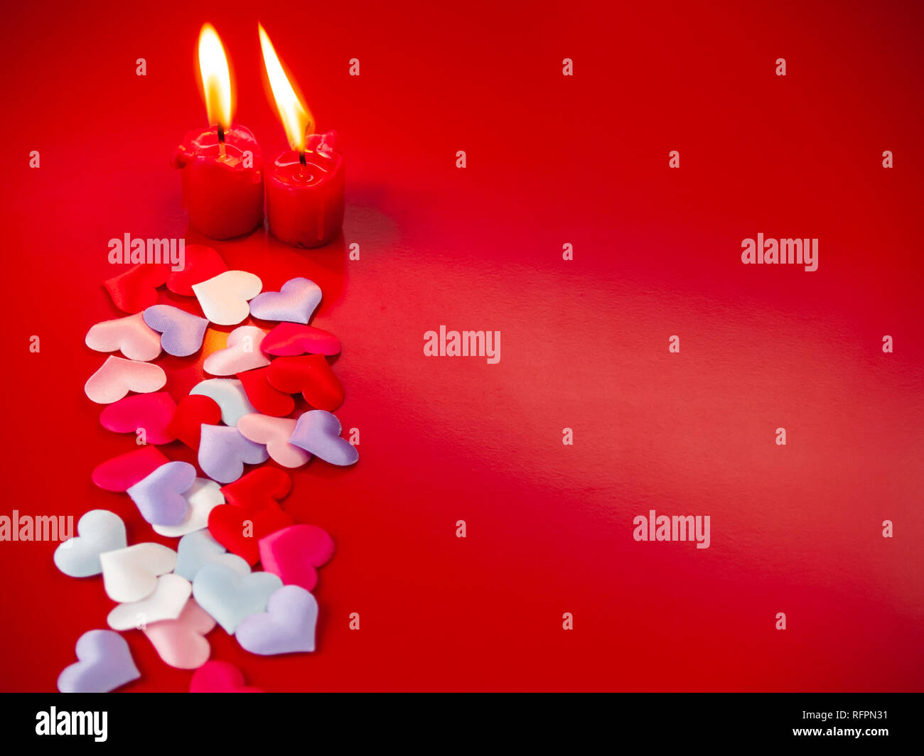 Concetto di amore candele rosse accese e un sacco di cuori multicolore con uno sfondo rosso Foto Stock