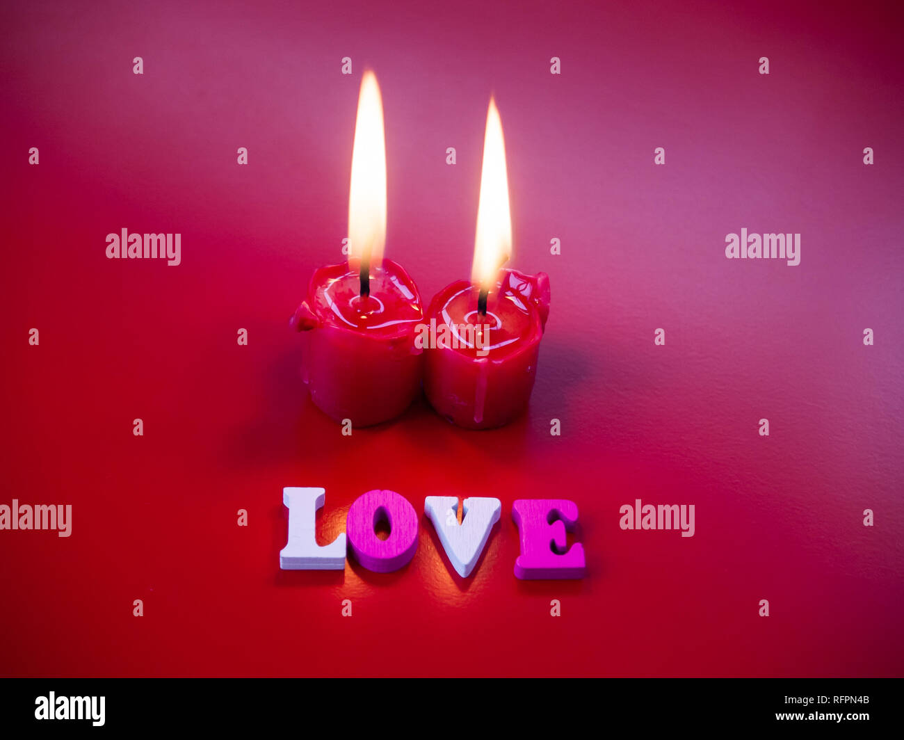 Concetto di amore candele rosse accese e la parola amore con uno sfondo rosso Foto Stock
