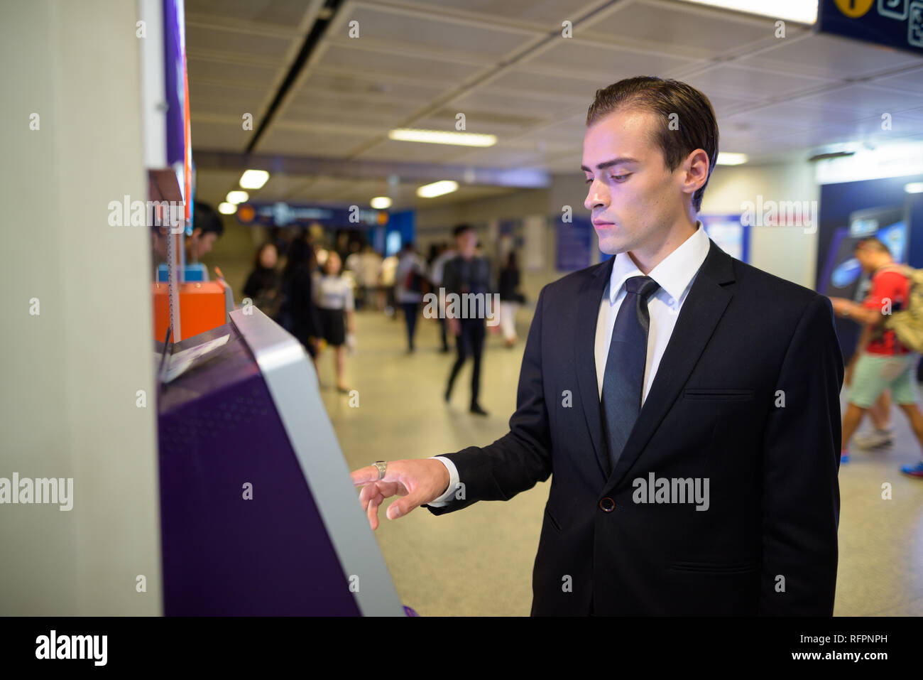 Giovane imprenditore tramite bancomat presso stazione ferroviaria Foto Stock